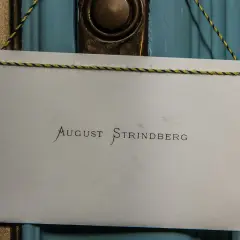En skylt med texten "August Strindberg" hänger på en blå dörr, kanske vid Strindbergsmuseet.