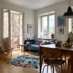 Ett vardagsrum med 60-tals inredning, färgglad matta, blå soffa och en gungstol. Utanför syns en balkong.