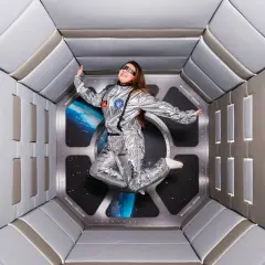 En person i rymddräkt svävar i en futuristisk tunnel, en del av en museum illusion i Stockholm.