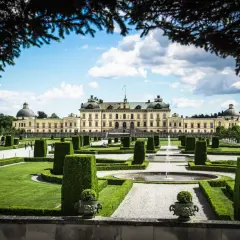 Drottningholms slottspark med fontäner och välklippta häckar. Kanske kungens båt ligger vid kajen, redo för en tur.