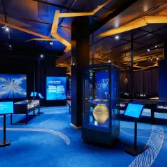 En utställning om historiska museet vikingar. Blå matta med vita mönster, montrar med föremål och skärmar med information.