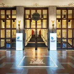 Entréhallen till Konserthuset Stockholm med en stor klocka ovanför trappan. Skyltar för Kungliga Filharmonikerna och Konserthuset Stockholm.