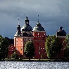 Mariefreds slott reser sig stolt vid vattnet, med sina röda tegelväggar och kupolformade tak under en dramatisk himmel.