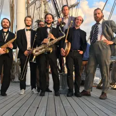 Ett storbandsjazz-band i Stockholm, med musiker som spelar saxofon, trumpet och banjo, poserar på ett fartyg.