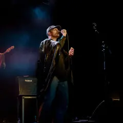 Mac DeMarco sjunger på scen i Stockholm, iklädd keps och en glansig jacka. En basist och en gitarrist syns också.