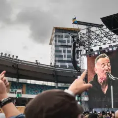 Publiken njuter av en Bruce Springsteen konsert i Sverige. En storbildsskärm visar The Boss sjunga medan fansen gestikulerar.