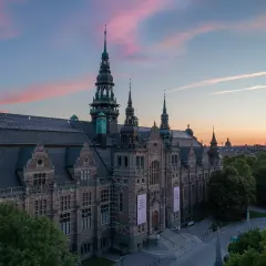 Nordiska museet badar i rosa kvällsljus. Imponerande arkitektur med torn och detaljer.