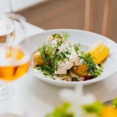 En vacker fiskrätt med potatis, ärtor och dill serveras på en vit tallrik. En perfekt måltid på Waldemarsudde restaurang.