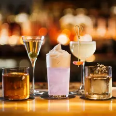 Fyra drinkar på en bänk, en martini, en rosa drink med skum, en ljus drink med en blomma och en bärnstensfärgad drink. En perfekt kväll på Hallwylska bar.