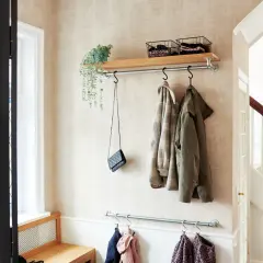 Långsmal hall inspiration med klädhängare, hylla med korgar och en väska. En bänk i trä syns till vänster.