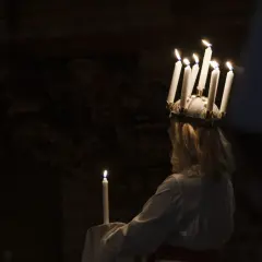 En flicka med ljus i håret, en traditionell Storkyrkan Lucia, håller ett ljus i mörkret.