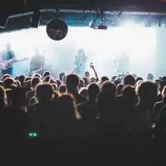 Publik njuter av en gratis konsert med bandet på scenen, upplyst av starka lampor och en discokula.