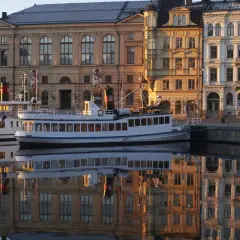 Fartyg i hamnen speglas i vattnet framför byggnader som vittnar om musikaliska Stockholm.