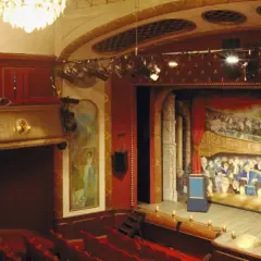 Teater Odenplan med sin pampiga scenmålning av publik i loger. Röda sammetssoffor och gyllene detaljer skapar en klassisk atmosfär.