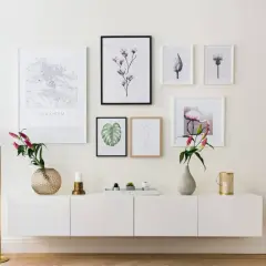 Ett modernt, vitt sideboard med konstverk ovanför, inklusive en Stockholmskarta och en flamingo. En golvlampa och vaser ger en stilfull touch.