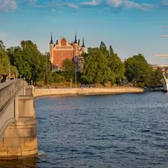 En vacker scen i Stockholm med en bro i förgrunden, ett rött tornliknande hus och ett stort vitt segelfartyg i vattnet.
