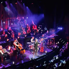 En orkester spelar på en scen i Stockholm, med en sångare i förgrunden. En levande revyupplevelse.