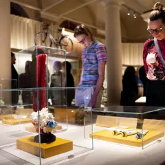Besökare på muzeum nobla beundrar utställningar i glasmonter, inklusive en röd scarf och molekylmodeller.