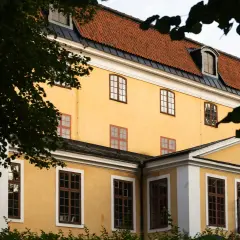 Gula fasaden på Ulriksdals teater med tegeltak och mörkgröna trädgrenar som ramar in.