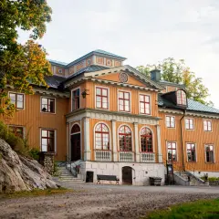 Vackert gul träbyggnad med röda fönster och tak, Rastaborgs slott, omgivet av höstfärgad grönska.