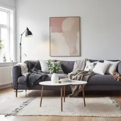 En grå soffa med kuddar och plädar i bohemisk stil. Ett runt soffbord med en vas och en matta med fransar.