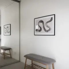 En hall med en grå bänk och en spegelvägg. Konst på väggen ger hall inspiration.
