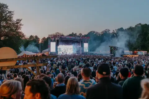 Stor publik vid Rosendal Garden Party. En stor scen med artister och ljusspel, omgiven av träd och tält.