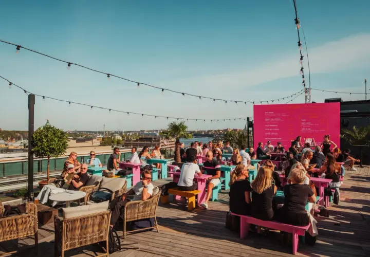 Folk njuter av solen och utsikten på en takbar i Stockholm. En perfekt plats för ett sommarevenemang.