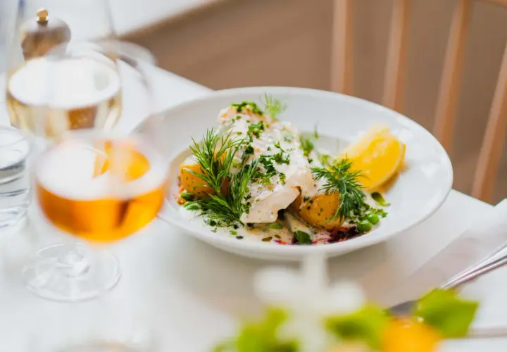 En vacker fiskrätt med potatis, ärtor och dill serveras på en vit tallrik. En perfekt måltid på Waldemarsudde restaurang.
