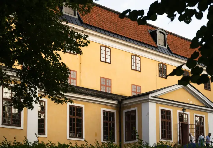 Gula fasaden på Ulriksdals teater med tegeltak och mörkgröna trädgrenar som ramar in.