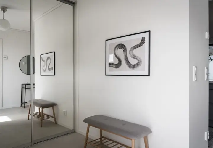 En hall med en grå bänk och en spegelvägg. Konst på väggen ger hall inspiration.