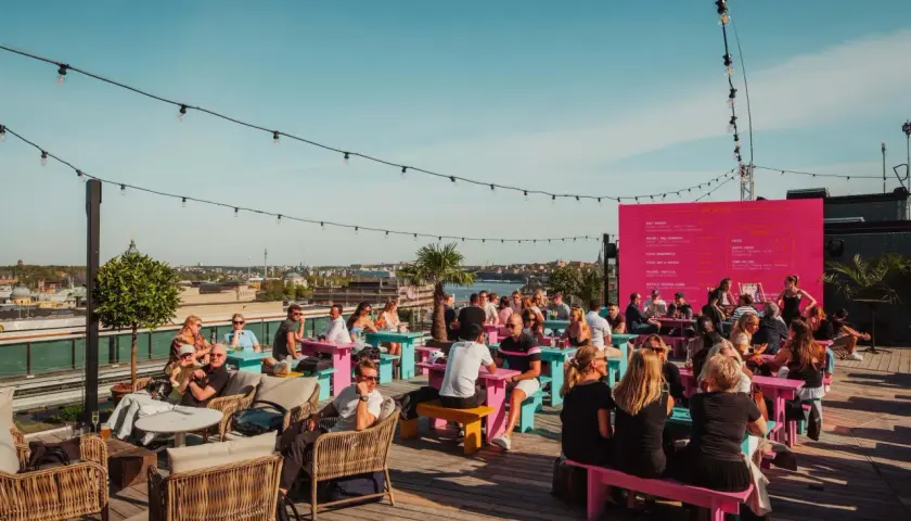 Folk njuter av solen och utsikten på en takbar i Stockholm. En perfekt plats för ett sommarevenemang.