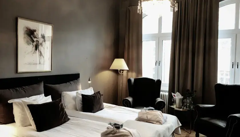 Ett elegant hotellrum med dubbelsäng, konst på väggen och en kristallkrona. Mysig hotellrum inredning med fåtöljer och en champagnehink.