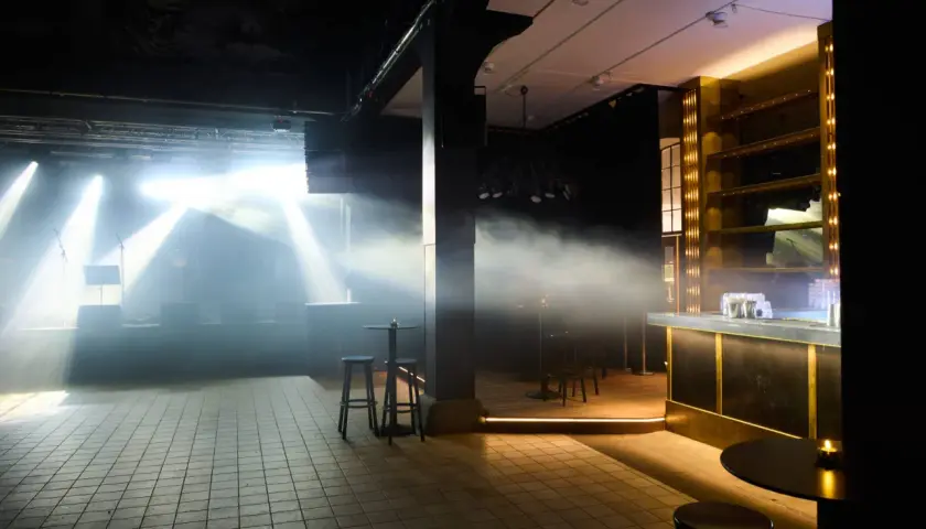 Scenljus och rök fyller lokalen på slaktkyrkan Stockholm. En bar i guld och svart syns till höger.