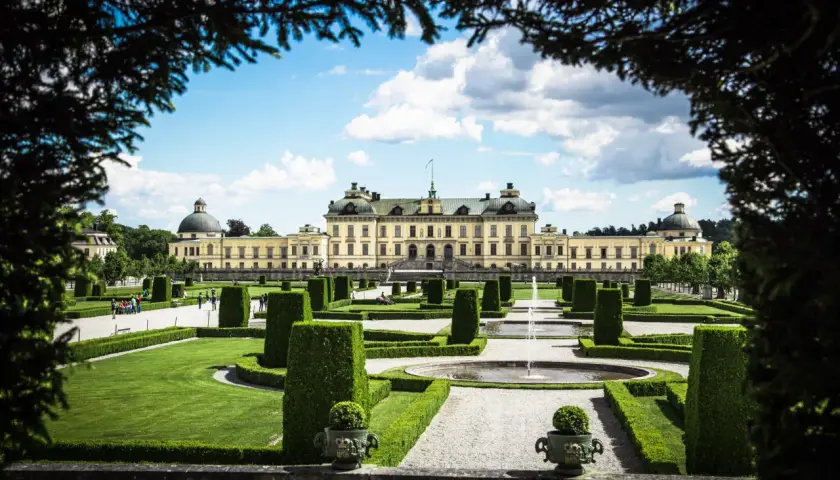 Drottningholms slottspark med fontäner och välklippta häckar. Kanske kungens båt ligger vid kajen, redo för en tur.