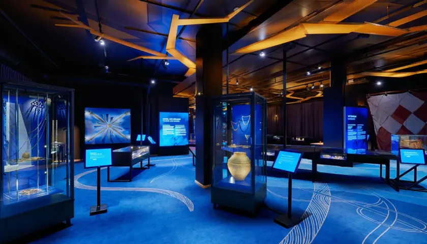 En utställning om historiska museet vikingar. Blå matta med vita mönster, montrar med föremål och skärmar med information.