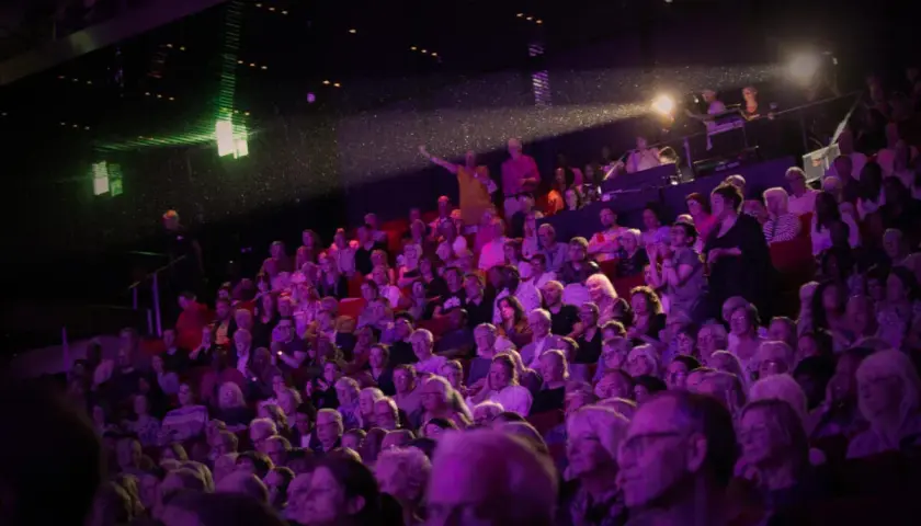 Publik njuter av en konsert i Uppsala. Scenen badar i lila ljus, och en artist gestikulerar mot publiken.