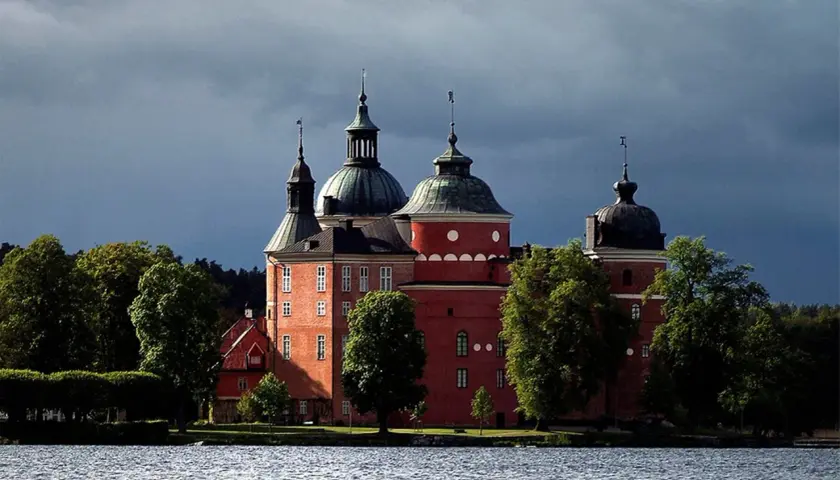 Mariefreds slott reser sig stolt vid vattnet, med sina röda tegelväggar och kupolformade tak under en dramatisk himmel.