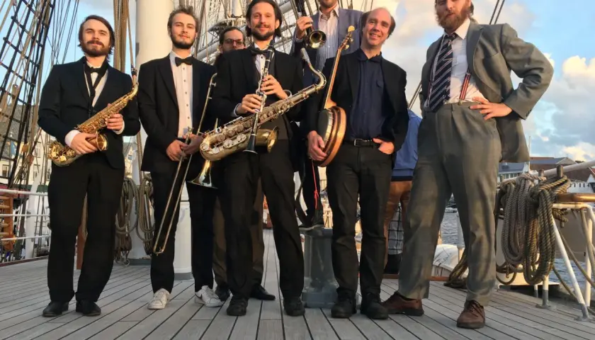 Ett storbandsjazz-band i Stockholm, med musiker som spelar saxofon, trumpet och banjo, poserar på ett fartyg.