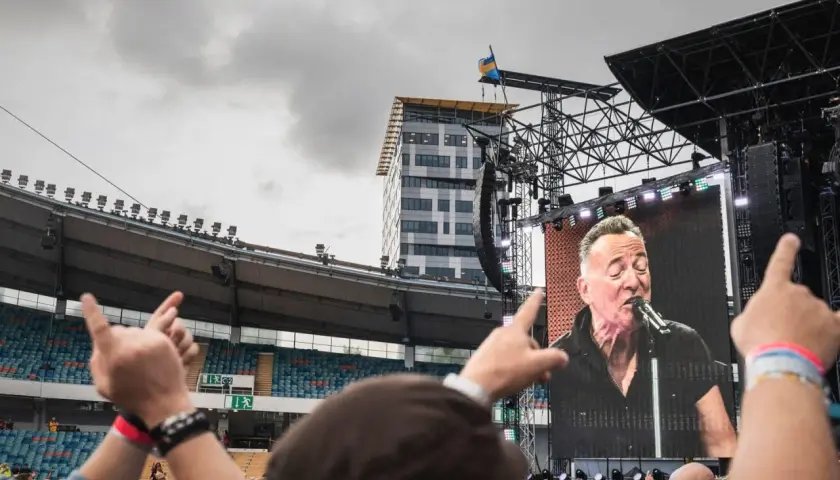 Publiken njuter av en Bruce Springsteen konsert i Sverige. En storbildsskärm visar The Boss sjunga medan fansen gestikulerar.