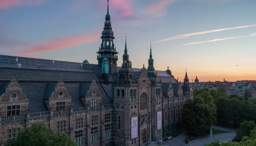 Nordiska museet badar i rosa kvällsljus. Imponerande arkitektur med torn och detaljer.