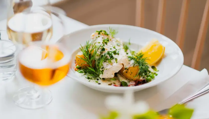 En vacker fiskrätt med potatis, ärtor och dill serveras på en vit tallrik. En perfekt måltid på Waldemarsudde restaurang.