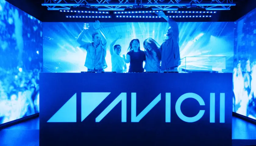 Glada besökare njuter av en upplevelse med Avicii-logotypen belyst i blått.