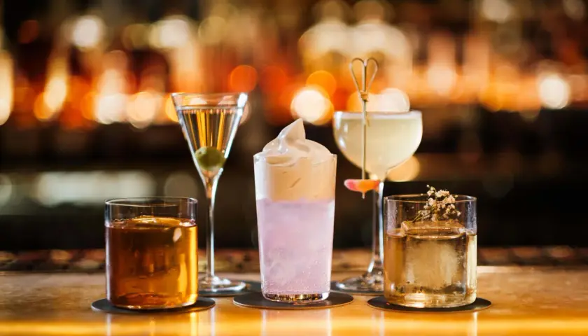 Fyra drinkar på en bänk, en martini, en rosa drink med skum, en ljus drink med en blomma och en bärnstensfärgad drink. En perfekt kväll på Hallwylska bar.