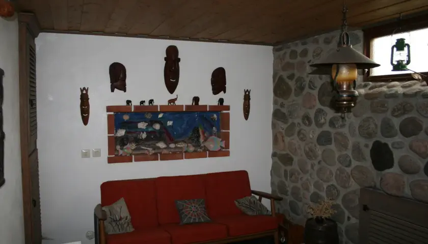 Gillestuga inspiration med en röd soffa, konstverk med afrikanska masker och stenklädd vägg.