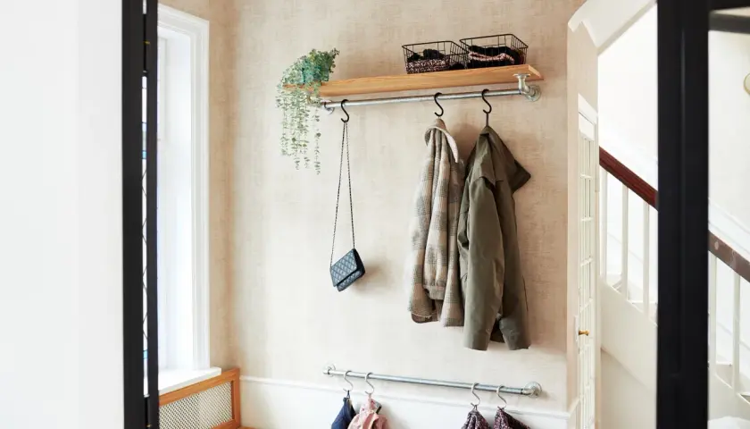 Långsmal hall inspiration med klädhängare, hylla med korgar och en väska. En bänk i trä syns till vänster.