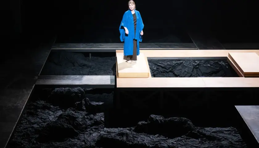 En kvinna i blå kappa står på en upphöjd plattform under en föreställning av Hamlet i Stockholm.