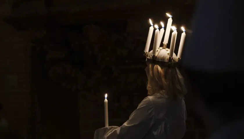 En flicka med ljus i håret, en traditionell Storkyrkan Lucia, håller ett ljus i mörkret.