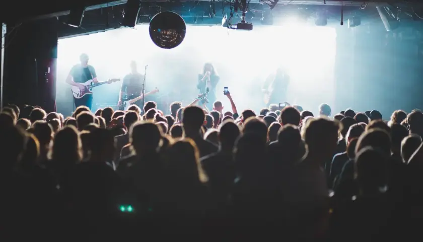 Publik njuter av en gratis konsert med bandet på scenen, upplyst av starka lampor och en discokula.