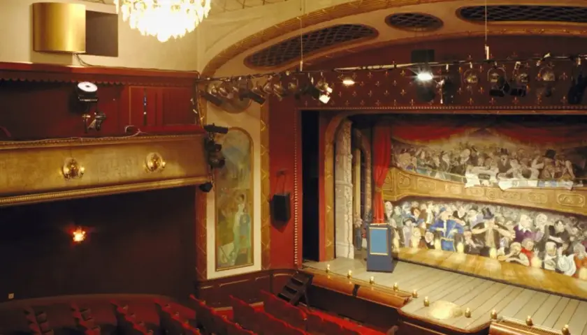 Teater Odenplan med sin pampiga scenmålning av publik i loger. Röda sammetssoffor och gyllene detaljer skapar en klassisk atmosfär.
